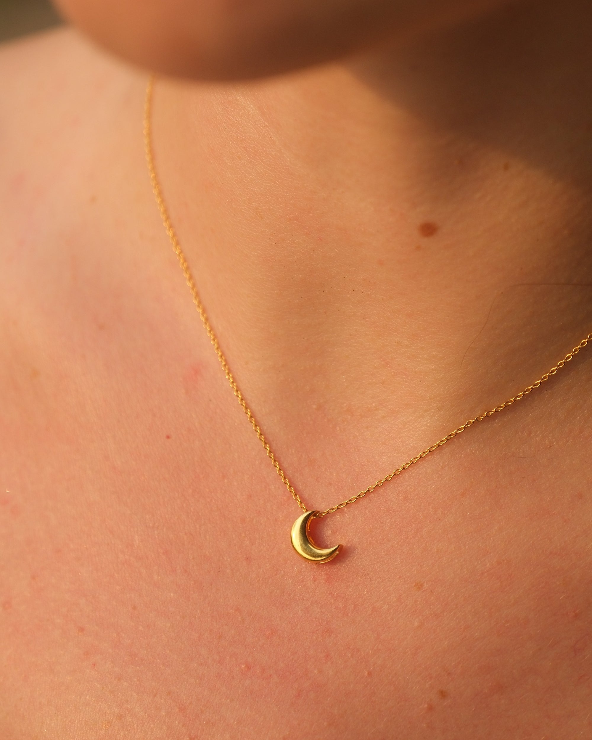 Gold necklace with a delicate 18KT gold vermeil crescent moon pendant on an adjustable chain, worn on a person’s neck.