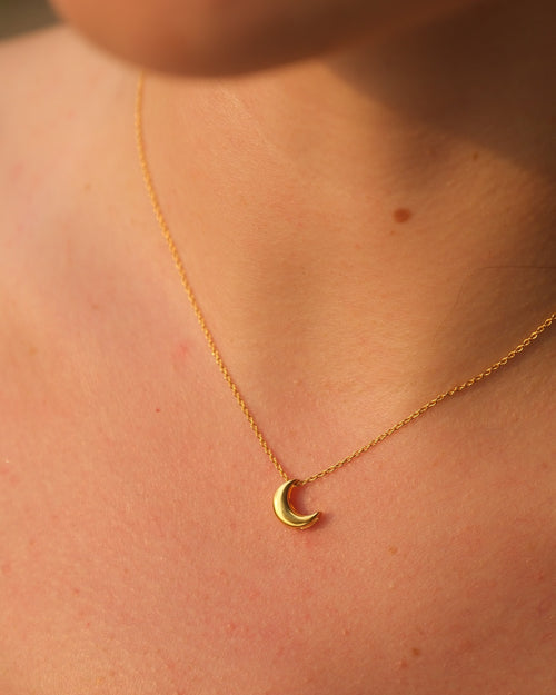 Gold necklace with a delicate 18KT gold vermeil crescent moon pendant on an adjustable chain, worn on a person’s neck.