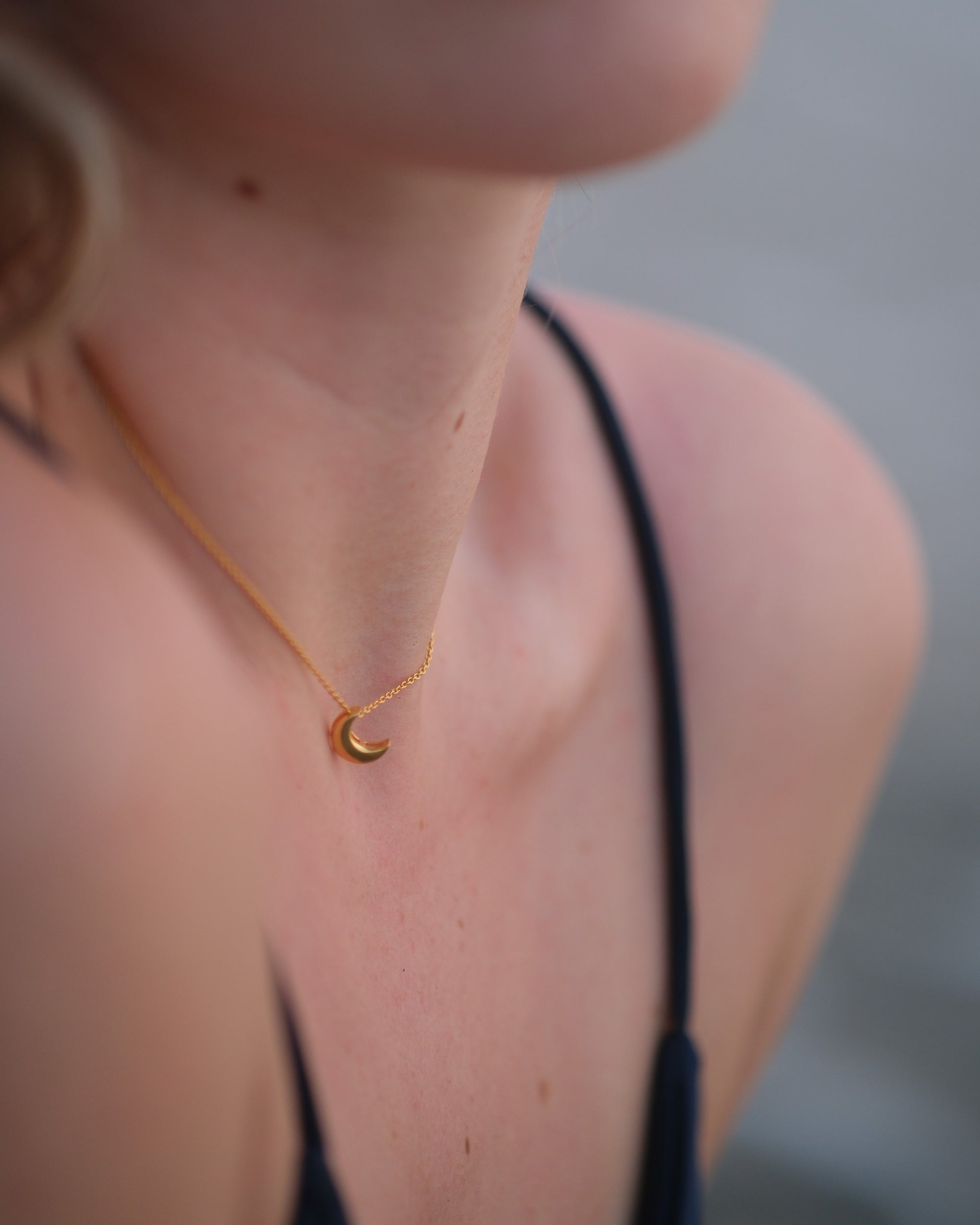 Handcrafted gold moon pendant necklace resting on a natural wooden surface, showcasing its smooth curve and fine craftsmanship.